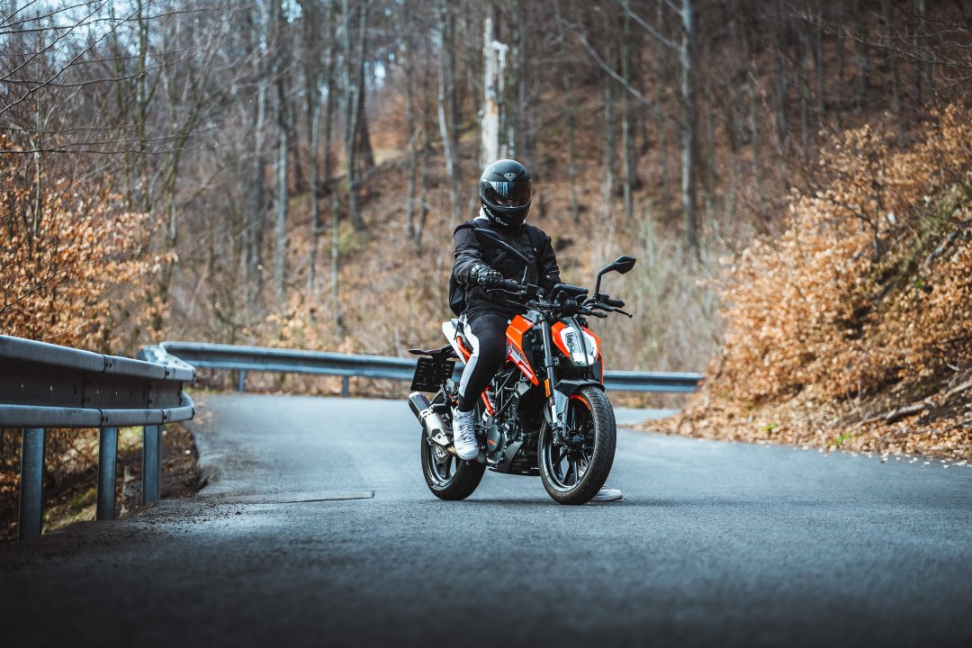 Homme se tenant sur une moto KTM Duke 125 orange au milieu d’une route de forêt