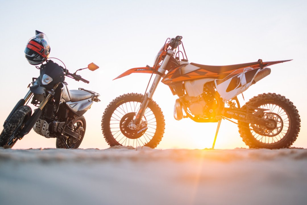Deux motos KTM garées devant un soleil couchant