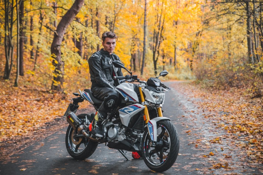 Jeune homme assis sur une moto roadster A2 sur une route de forêt
