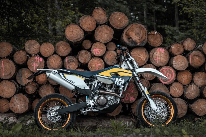 Moto supermotard Husqvarna garée devant des rondins de bois