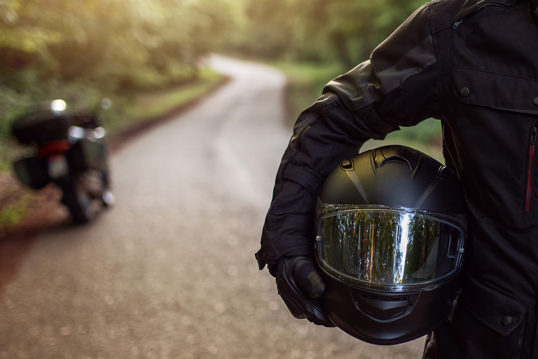 Motorcycle rider standing on the road holding a helmet