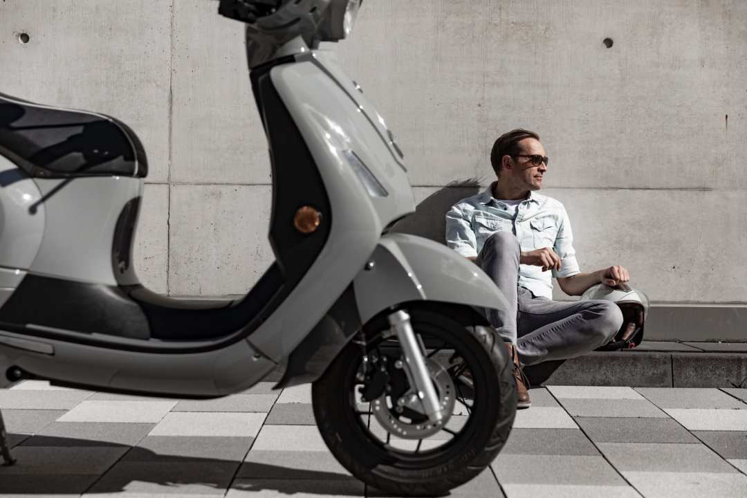 Homme assis à côté d’un scooter électrique de couleur grise