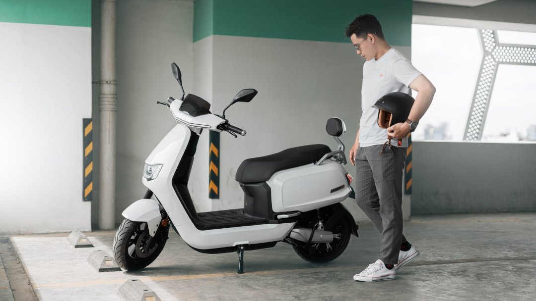 Homme se tenant près d’un scooter électrique de couleur blanche garé dans un parking